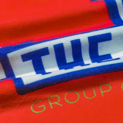 Close-up of a red custom printed towel featuring an embroidered logo with the text 'THE GROUP' in blue and white, highlighting personalized towels.